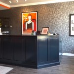 A modern dental reception area with a dark counter, patterned grey wallpaper, and vibrant orange accent walls featuring artistic portraits.
