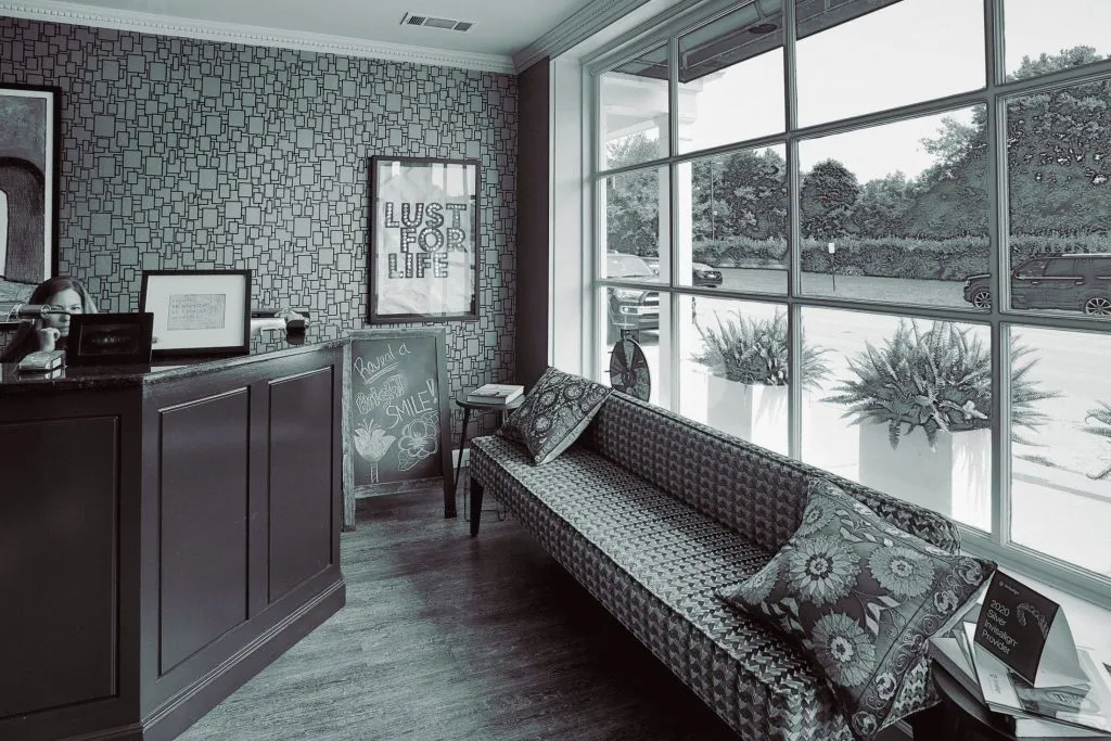 A stylish waiting area with a long patterned sofa, large windows, and contemporary decor in shades of grey and orange.