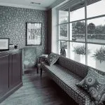 A stylish waiting area with a long patterned sofa, large windows, and contemporary decor in shades of grey and orange.