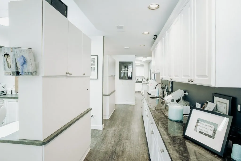 A clean, white clinical hallway with laboratory equipment and cabinetry organized for dental procedures.