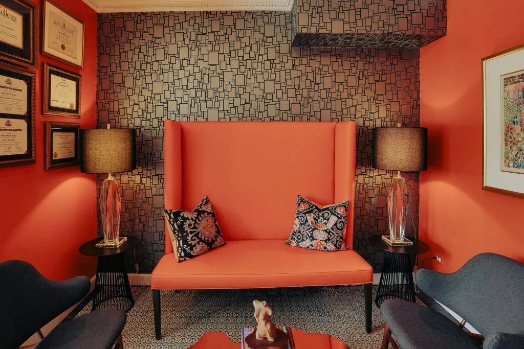 A high-back orange designer chair serving as a focal point in a waiting room with warm lighting and framed certificates.