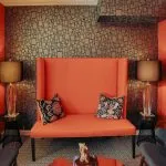 A high-back orange designer chair serving as a focal point in a waiting room with warm lighting and framed certificates.