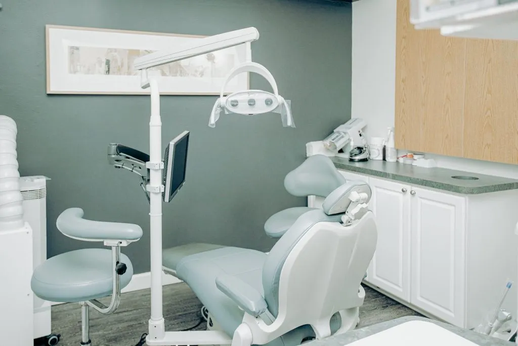 A modern dental operatory room with a light blue patient chair, white cabinetry, and teal accent walls.