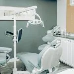 A modern dental operatory room with a light blue patient chair, white cabinetry, and teal accent walls.