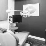 A dental treatment room with a minimalist aesthetic, featuring a grey patient chair against a dark grey wall with lip-themed artwork.