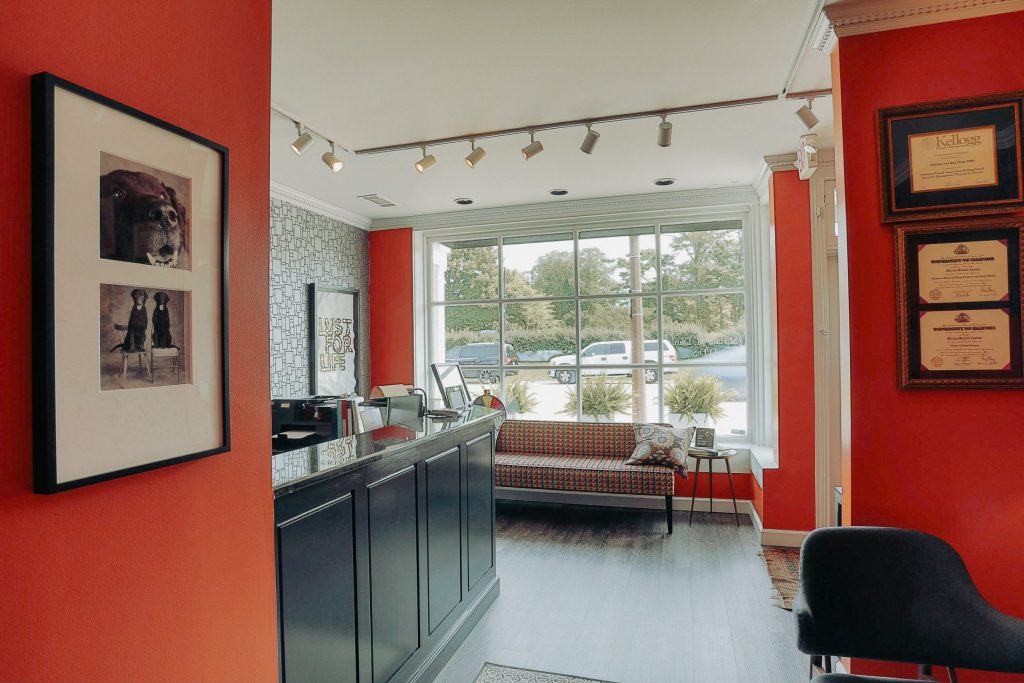Interior view of the reception desk area showcasing professional certificates on an orange wall and a glimpse of the patient lounge.