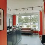 Interior view of the reception desk area showcasing professional certificates on an orange wall and a glimpse of the patient lounge.