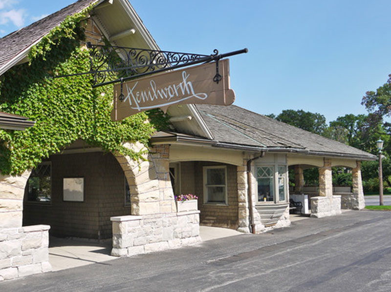 Exterior view of Martin Family Dentistry, a tan brick building with a prominent blue sign displaying the address 6130 Nieman Rd. next to a glass double-door entrance with white potted plants.