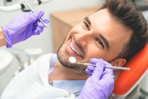 Man smiling while getting a dental exam with dental tools close to his mouth