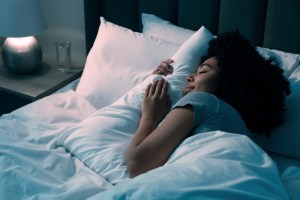 Young woman laying in bed and hugging a pillow, looking peaceful and slightly smiling with her eyes closed